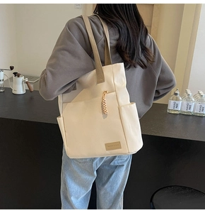 Detail of canvas tote bag with side pocket, brown strap and fashion label on the front