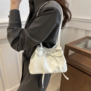 Minimalist white bucket bag with large bow drawstring detail shown on shoulder