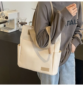 Detail of minimalist beige canvas tote bag with side pocket and brown leather tag