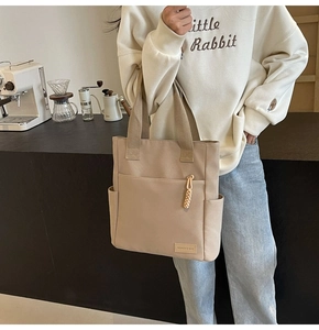 Detail view of khaki canvas tote bag featuring multi-pocket design and fashion woven label