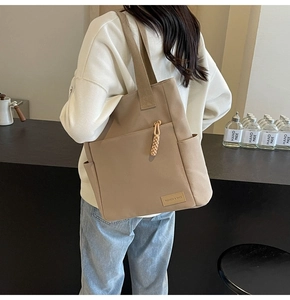 Detail of khaki canvas tote bag featuring a large front zipper pocket and side open pocket