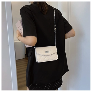 Détail du sac à bandoulière blanc matelassé avec chaîne argentée porté sur un blazer noir