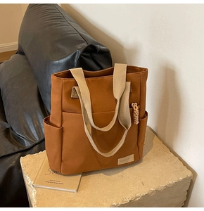 Detail of a brown canvas tote bag featuring beige webbing handles and a fashion label