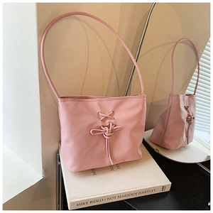 Détail d'un sac seau rose clair avec un design à lacets croisés sur un livre