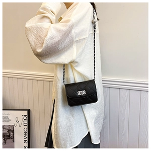 Détail d'un sac à bandoulière noir matelassé avec chaîne argentée porté par un mannequin