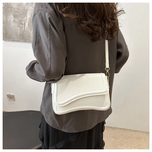 Back view of a model wearing a white crossbody bag with wave flap and gold buckle detail