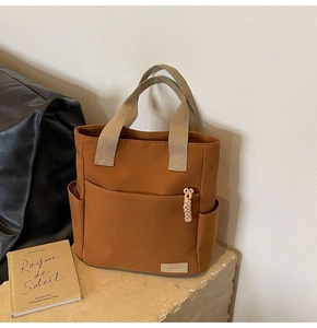 Detail view of brown canvas tote bag featuring wide beige straps and side storage pockets