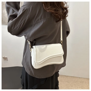 Minimalist white crossbody bag with wave-edge flap shown on model in modern interior