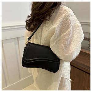 Black leather shoulder bag with wavy flap design and gold hardware shown on model