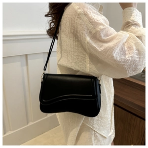 Detail of minimalist black crossbody bag featuring a unique wavy flap and golden hardware