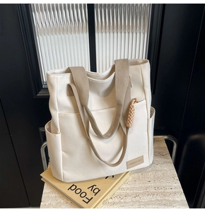 Close-up of cream canvas tote bag showing khaki woven handle and leather logo patch