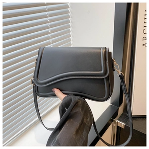 Detail of black crossbody bag featuring unique irregular wave curved flap and gold hardware