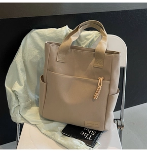 Detail of khaki tote bag with front pocket, side pockets, and woven tassel ornament
