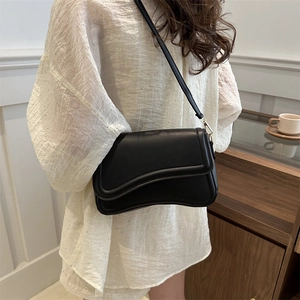 Minimalist black crossbody bag with unique wave-cut flap design worn by model in home setting