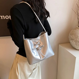 Sac à bandoulière argenté métallisé avec nœud porté par un mannequin en décor moderne