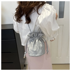 Detailed close-up of a silver metallic drawstring bucket bag with pleated texture and thin straps