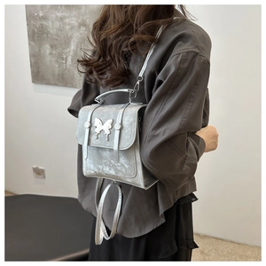 Close-up of metallic silver backpack featuring a decorative butterfly metal buckle detail