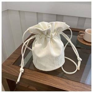 Close-up of a white textured drawstring bucket bag with elegant gold metal tips