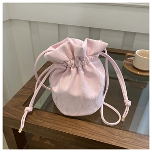 Detailed macro view of pink drawstring bucket bag with shiny textured fabric and gold metal tips