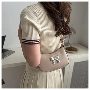 Chic beige crescent armpit bag with silver bow detail styled in a minimalist setting