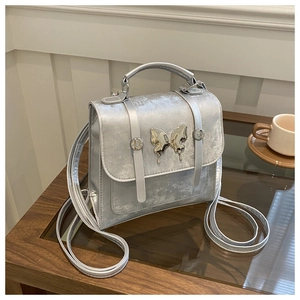 Detailed view of metallic silver handbag with a liquid metal butterfly buckle on the flap
