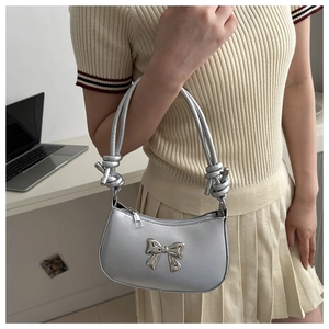Detail of silver metallic underarm bag with metal bow and knotted handle on shoulder