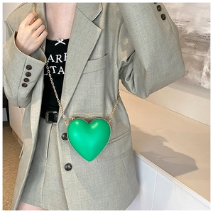 Détail d'un sac bandoulière vert en forme de cœur avec chaîne dorée sur costume vert