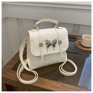 Detail of cream white bag featuring vintage jacquard pattern and silver butterfly ornament