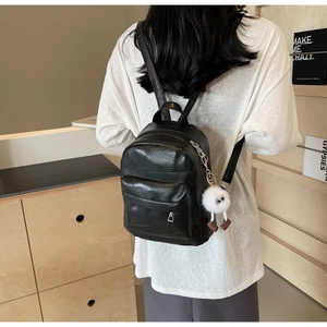 Detail of black mini backpack with leather texture and a cute white plush pendant