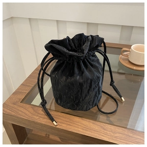 Detail of black pleated bucket bag with drawstring closure and golden hardware tips