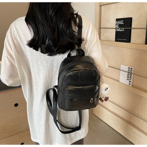 Close-up of black PU leather mini backpack with textured patchwork and soft plush pendant