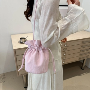 Pink drawstring bucket bag with satin texture shown on model in a modern interior setting