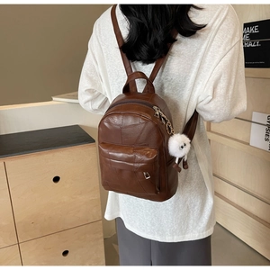 Detail of a brown leather mini backpack with a white plush pom-pom keychain and front pocket