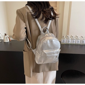 Detailed view of shiny silver metallic backpack with geometric texture and zip pocket