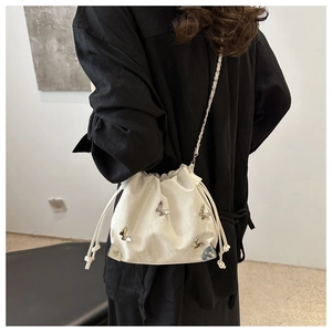 Detail of white leather drawstring bucket bag with silver butterfly charms and chain strap