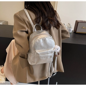 Detail of silver geometric backpack with plush monster charm and smooth side zipper