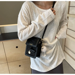 Close-up of black crossbody bag with gold fashion metal bar and white plush eye charm