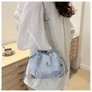 Detail of light blue bucket bag with silver butterflies and chain strap worn by person