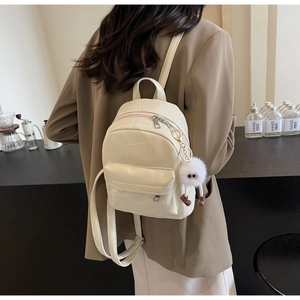 Close-up of cream leather backpack with crocodile pattern and plush monster charm