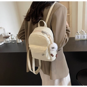 Mini cream backpack with quilted pattern and plush monster charm shown in a coffee shop