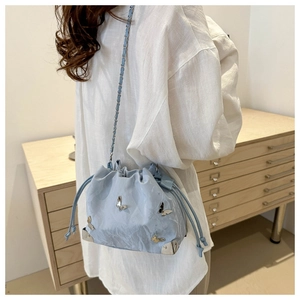 Detail of light blue bucket bag with silver butterfly and drawstring on model's shoulder