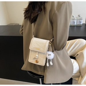 Close-up of off-white crossbody bag with gold Fashion logo and plush monster charm