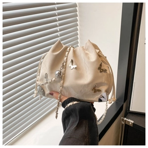 Detail of cream drawstring bucket bag featuring silver butterfly charms and chain strap