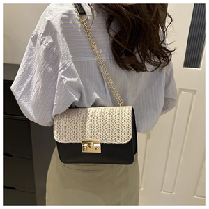Detailed close-up of a woven straw shoulder bag with elegant gold metal chain and lock