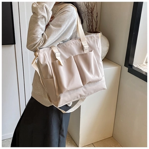 Detail of a large beige nylon tote bag featuring functional front pockets and adjustable strap