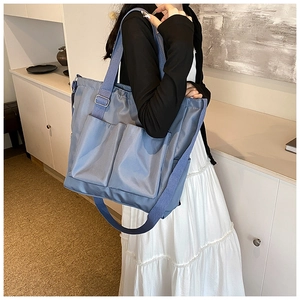 Detail view of a large light blue tote bag featuring functional front pockets and wide straps