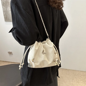 White bucket bag with silver butterfly charms and woven chain strap shown on model