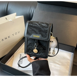 Detail of black textured crossbody phone bag in a premium gift box with plush charm