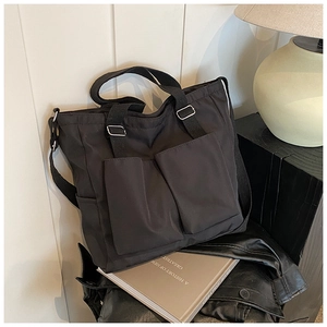 Detail of minimalist black nylon tote bag with dual front pockets and adjustable strap