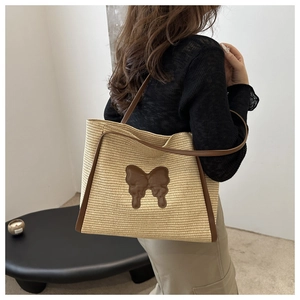 Detailed view of straw tote bag with brown leather handles and butterfly patch decoration